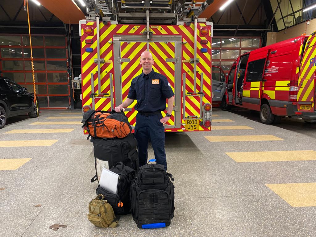Firefighter Rob Thomson standing in front of a fire engine with his bags, ready to fly to Malawi