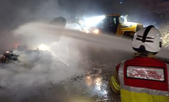 A fire officer oversees water being fired onto a pile of rubbish