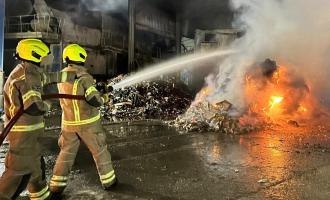 Two firefighters spraying water on a pile of rubbish which is on fire