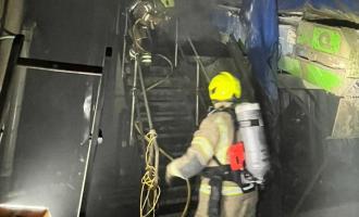 A firefighter at the bottom of a small set of stairs and a firefighter at the top of the stairs, both wearing breathing apparatus