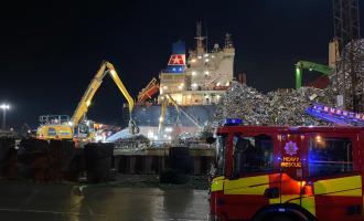 A fire engine next to the scene of a ship fire