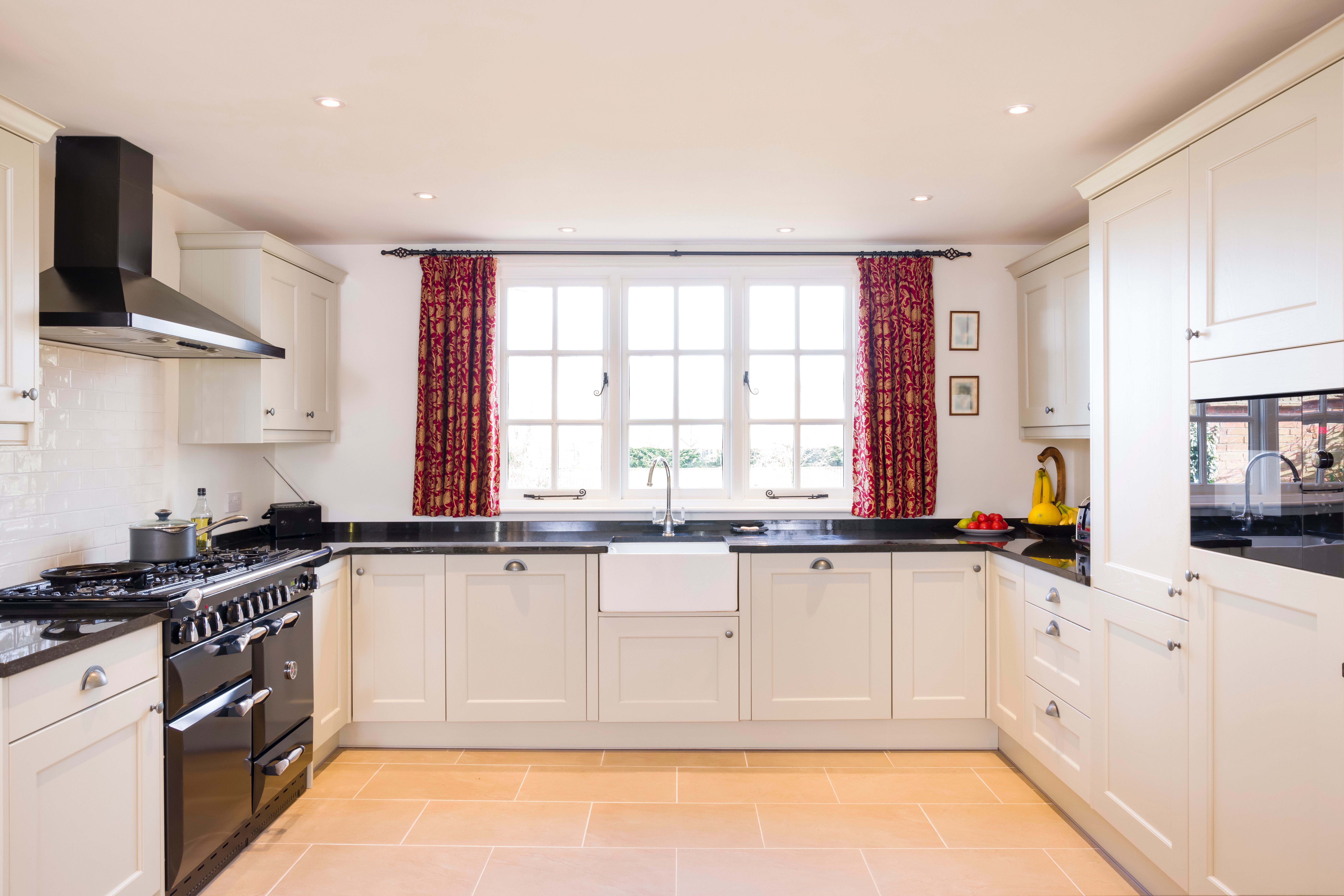 White kitchen with wooden floor, black worktops and red curtains