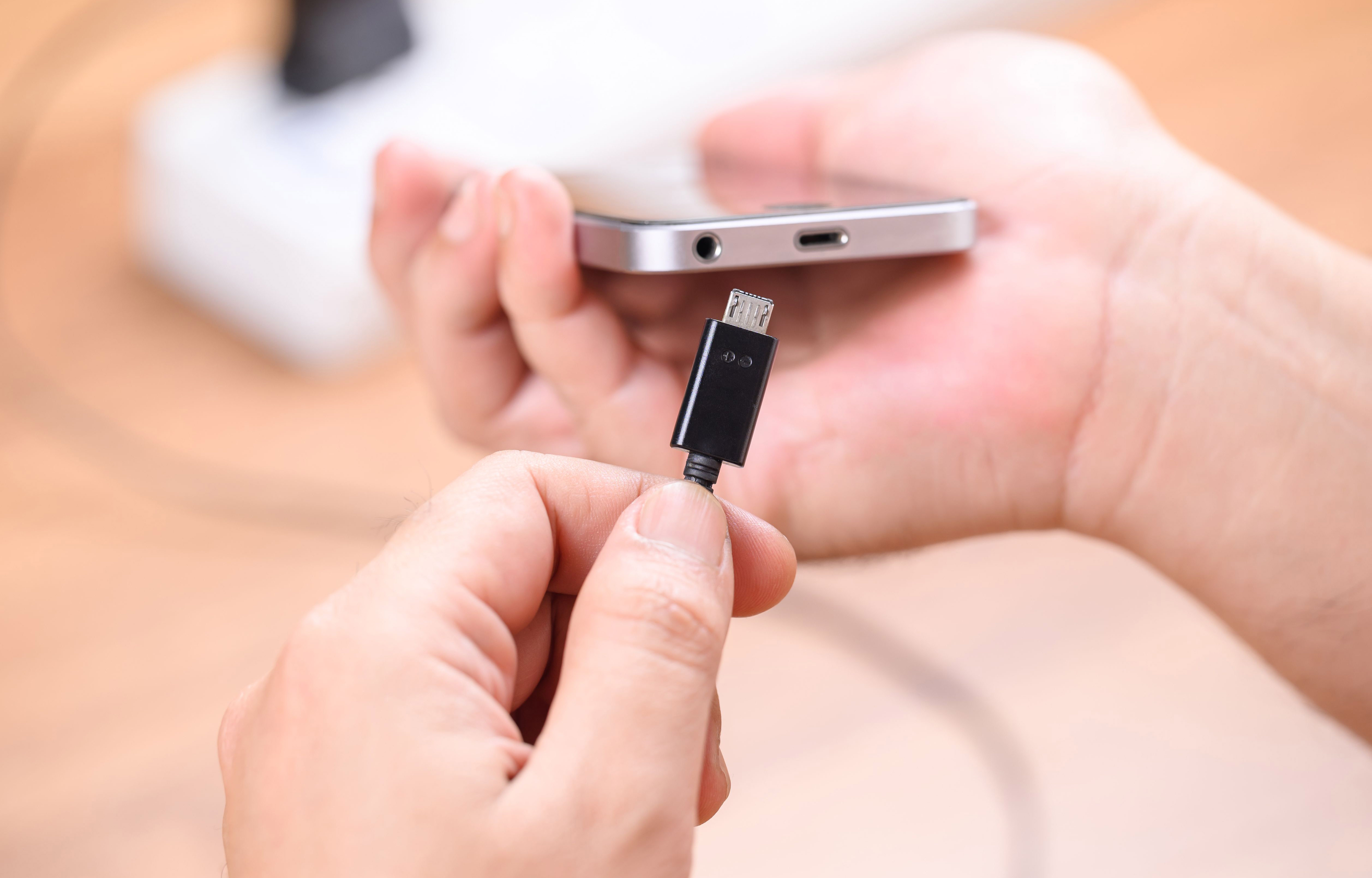 A hand holding a phone and the other hand placing a charger into the charging port