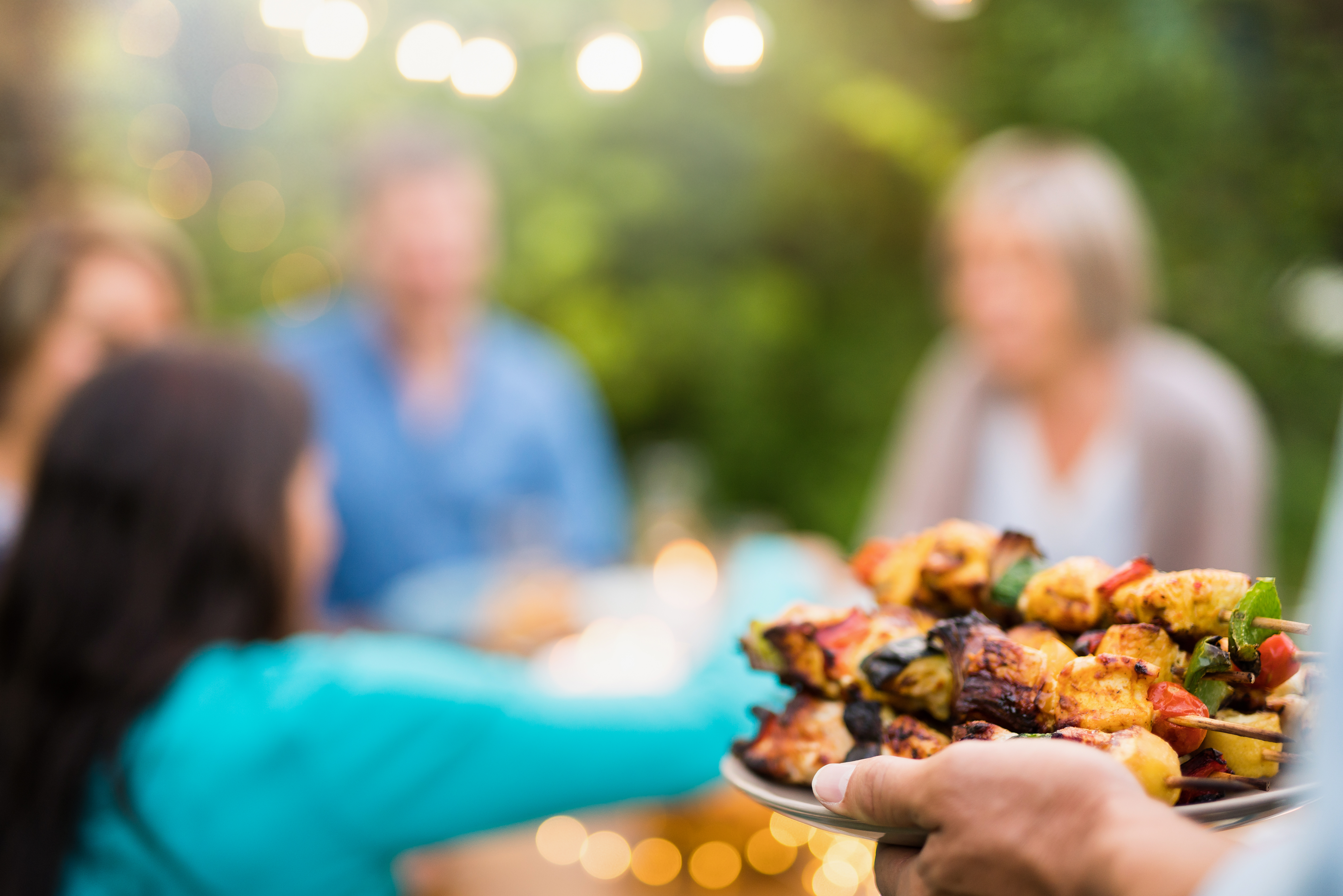 Plate of barbecued skewers being offered to group of friends in the distance