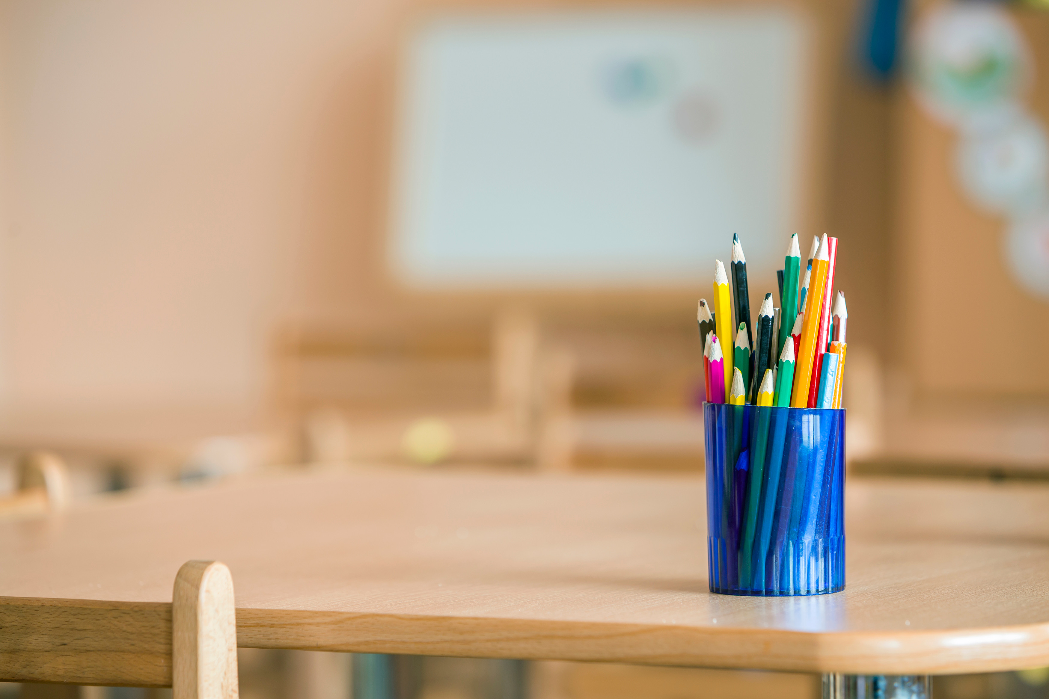 Blue pot filled with colouring pencils, set on wooden school desk