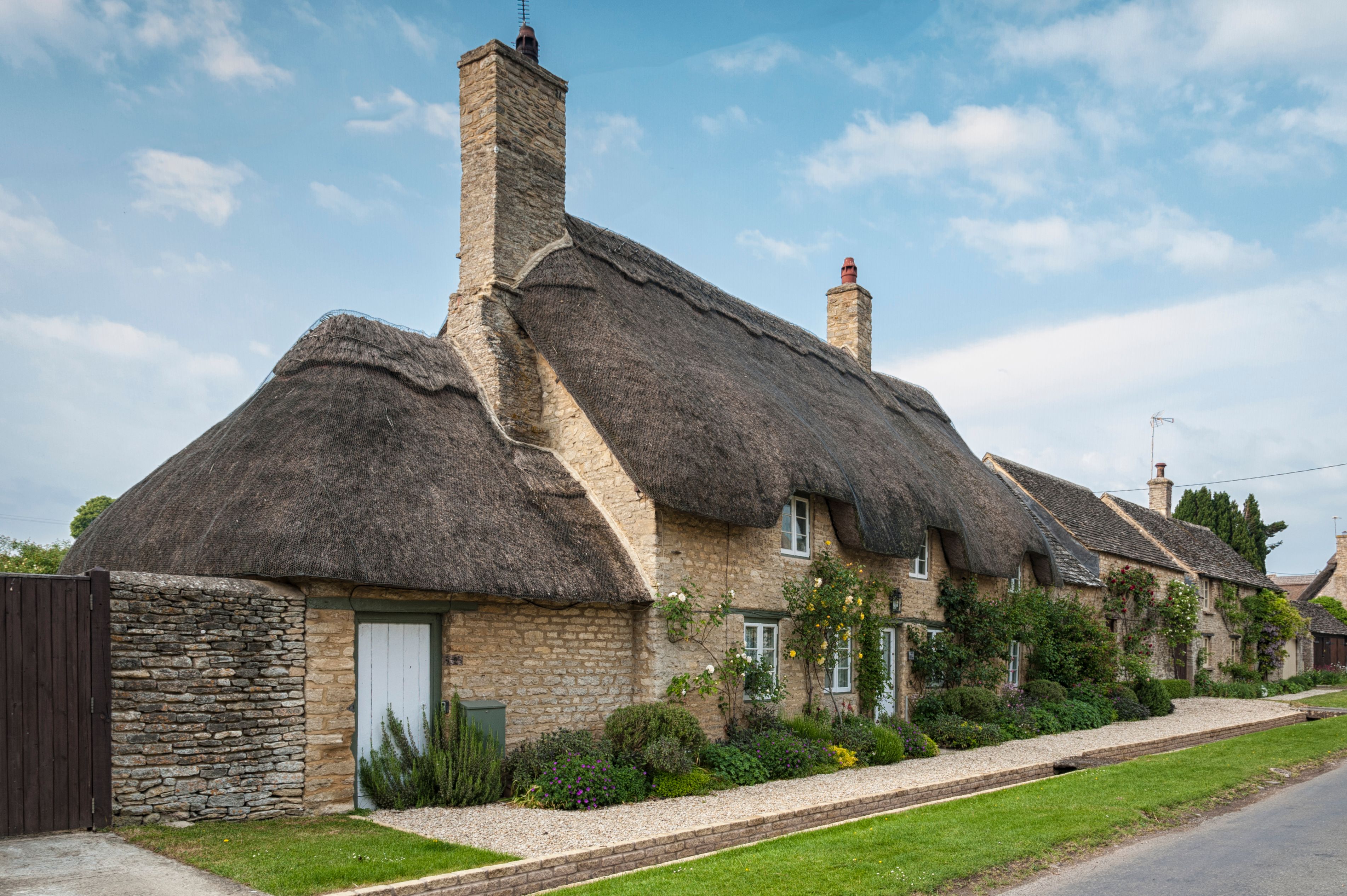 Thatched house with thatched garage. A grass verge separates the property from the road.