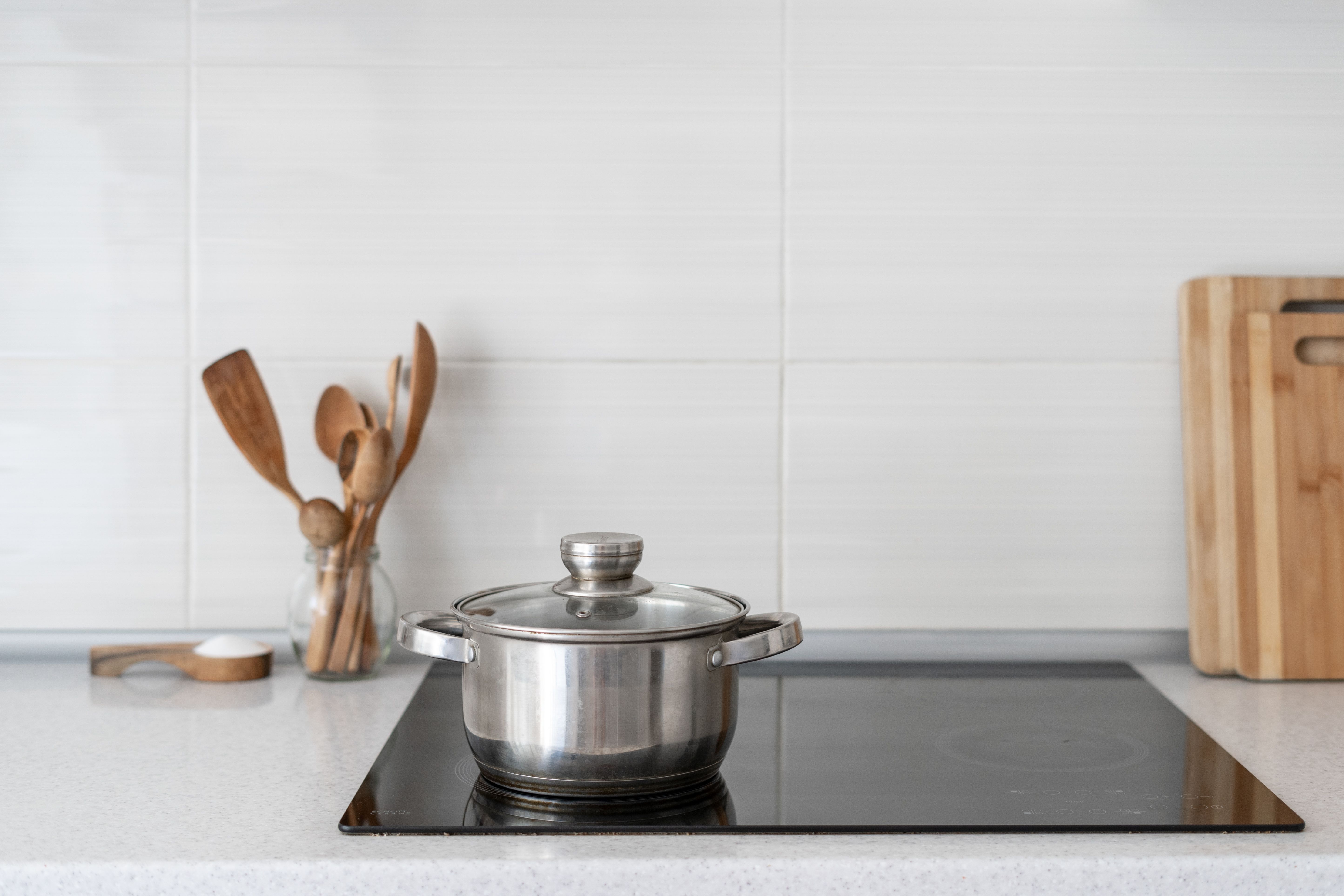 Stainless steel pan on induction hob. Wooden utensils and chopping board in the background