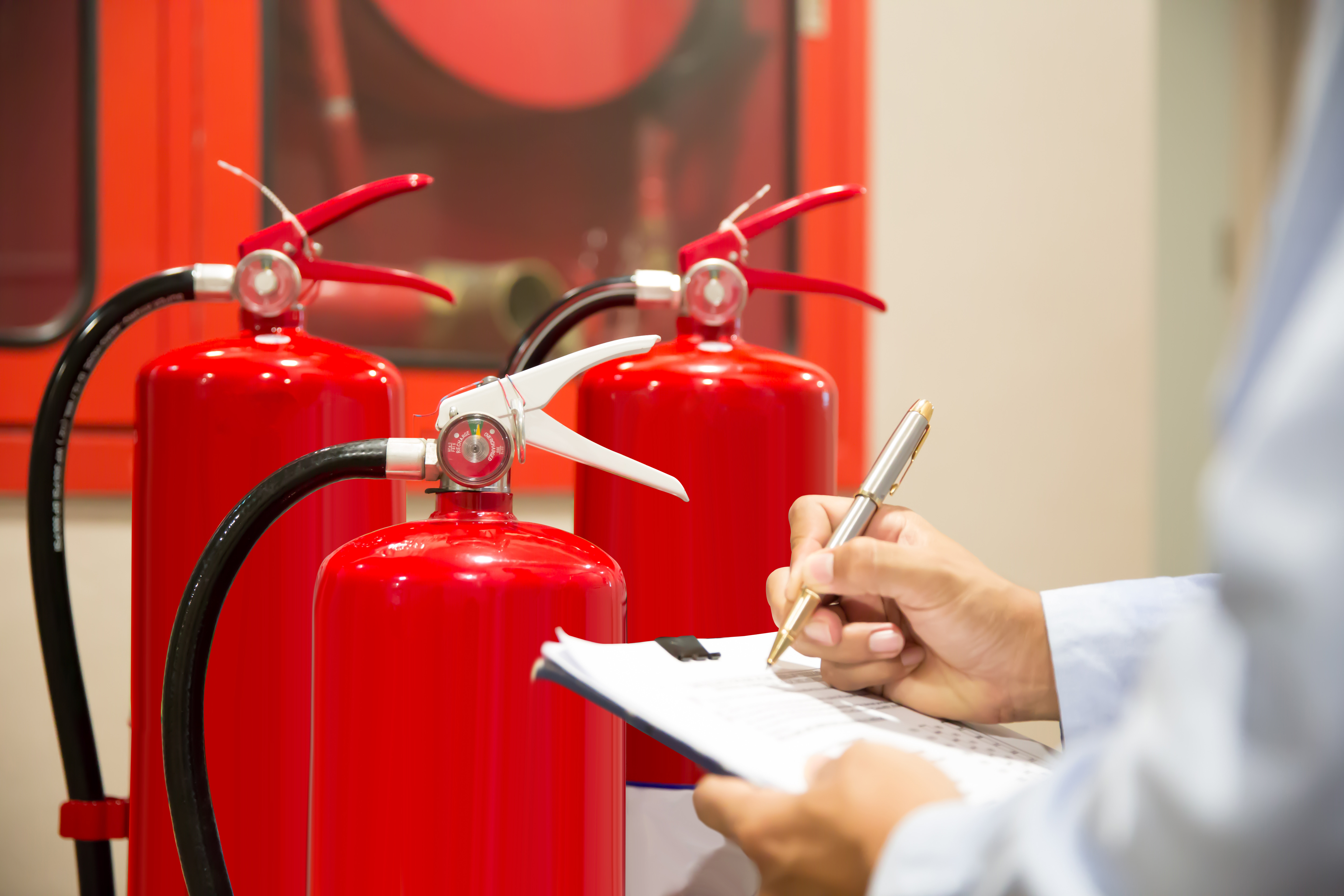 Three red fire extinguishers behind close up of man's arms holding a pen and a clipboard.