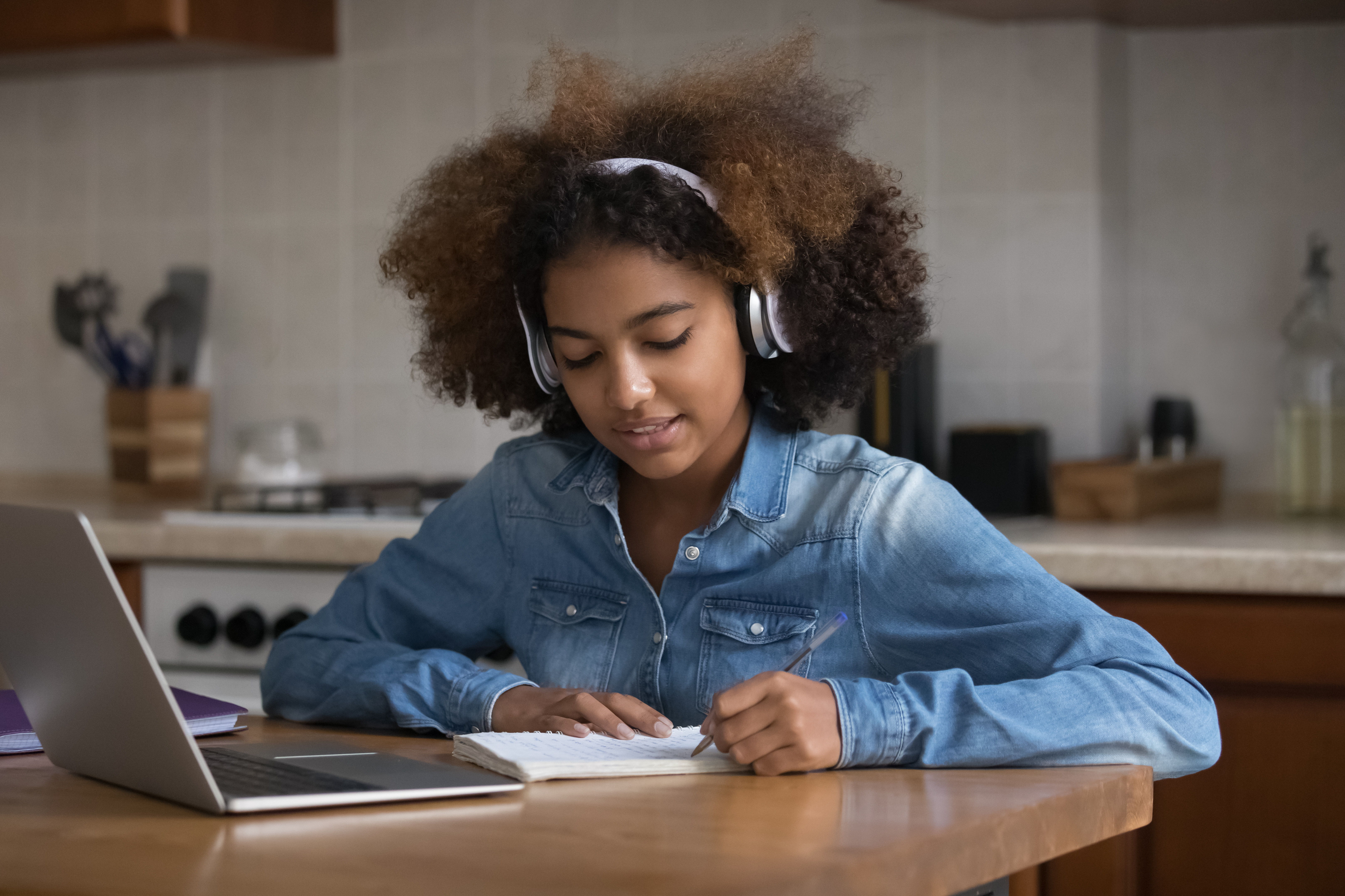 Teenage girl with headphones on sat at a laptop on a wooden table