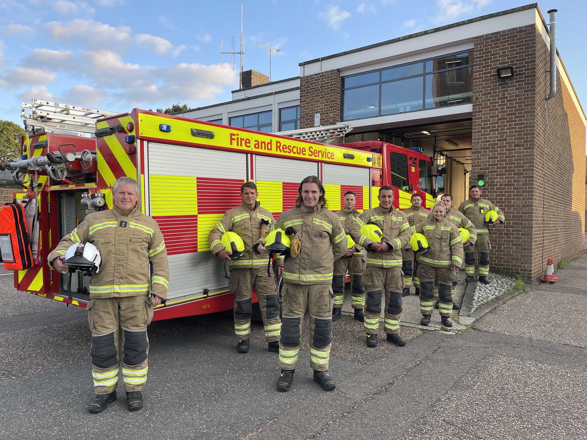 Eight crew members holding helmets next to fire engine