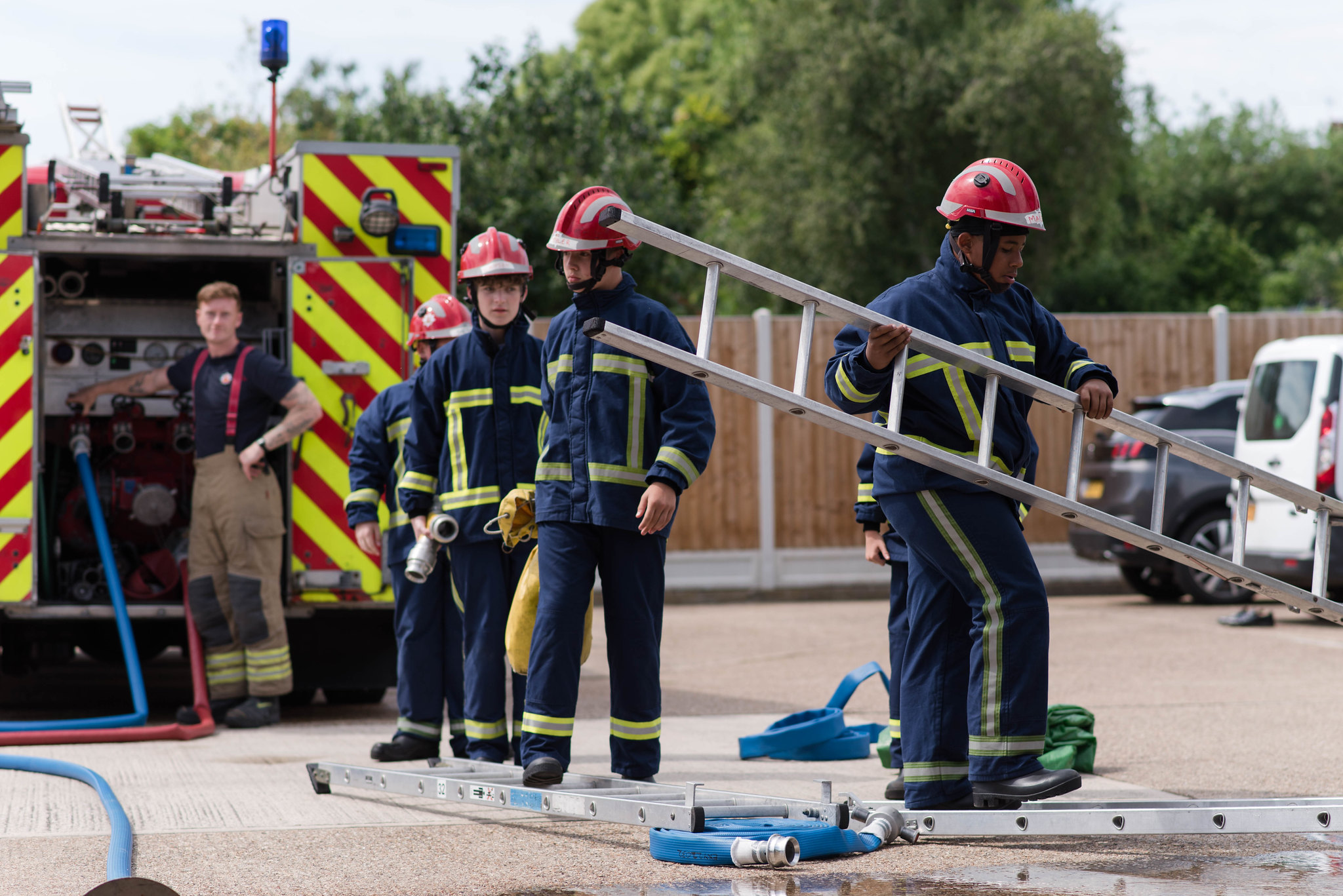 Four Fire Break participants, all boys in their teens, move a ladder across a forecourt at a fire station