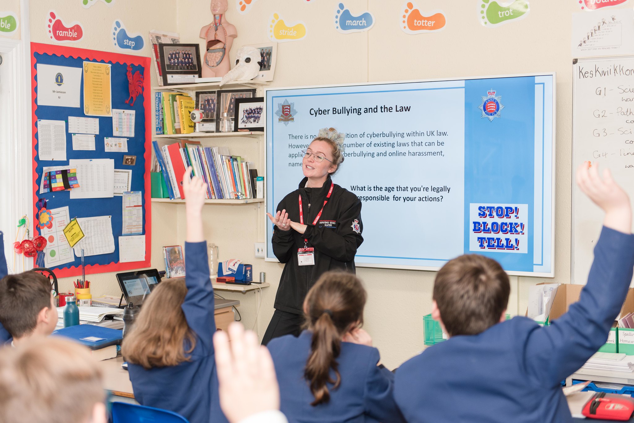 Education Officer standing by a projector in front of primary school children in blue uniform. One boy has raised his hand