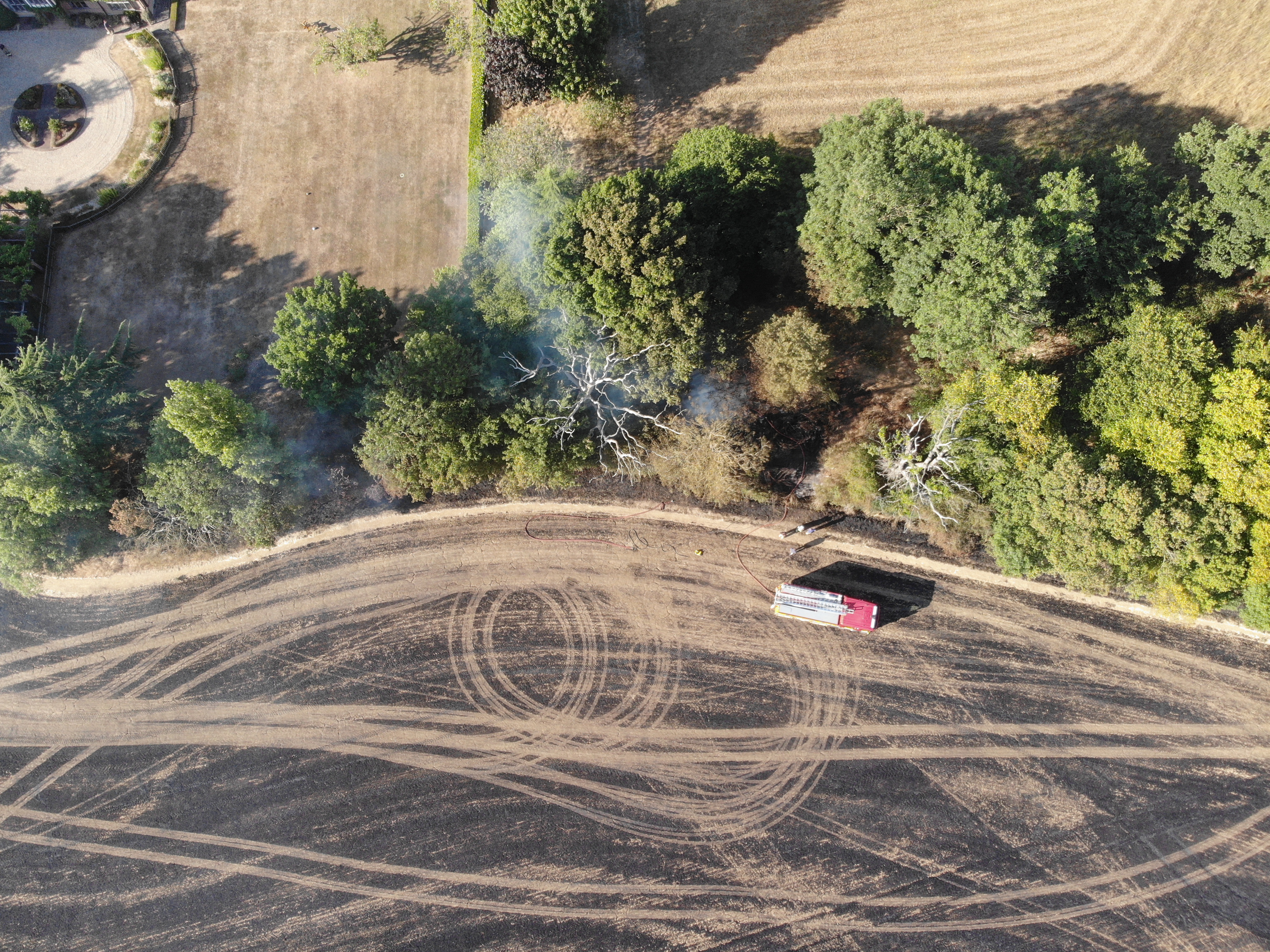 An aerial view of a burned field with a fire engine parked up.