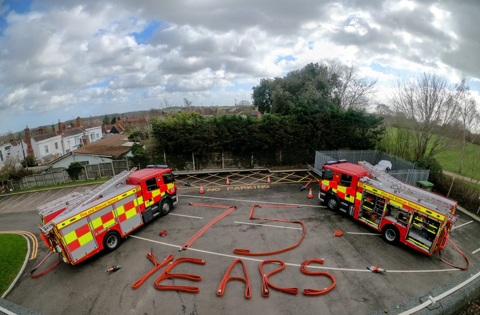 Two fire engines parked with '75 years' written using fire hoses. 