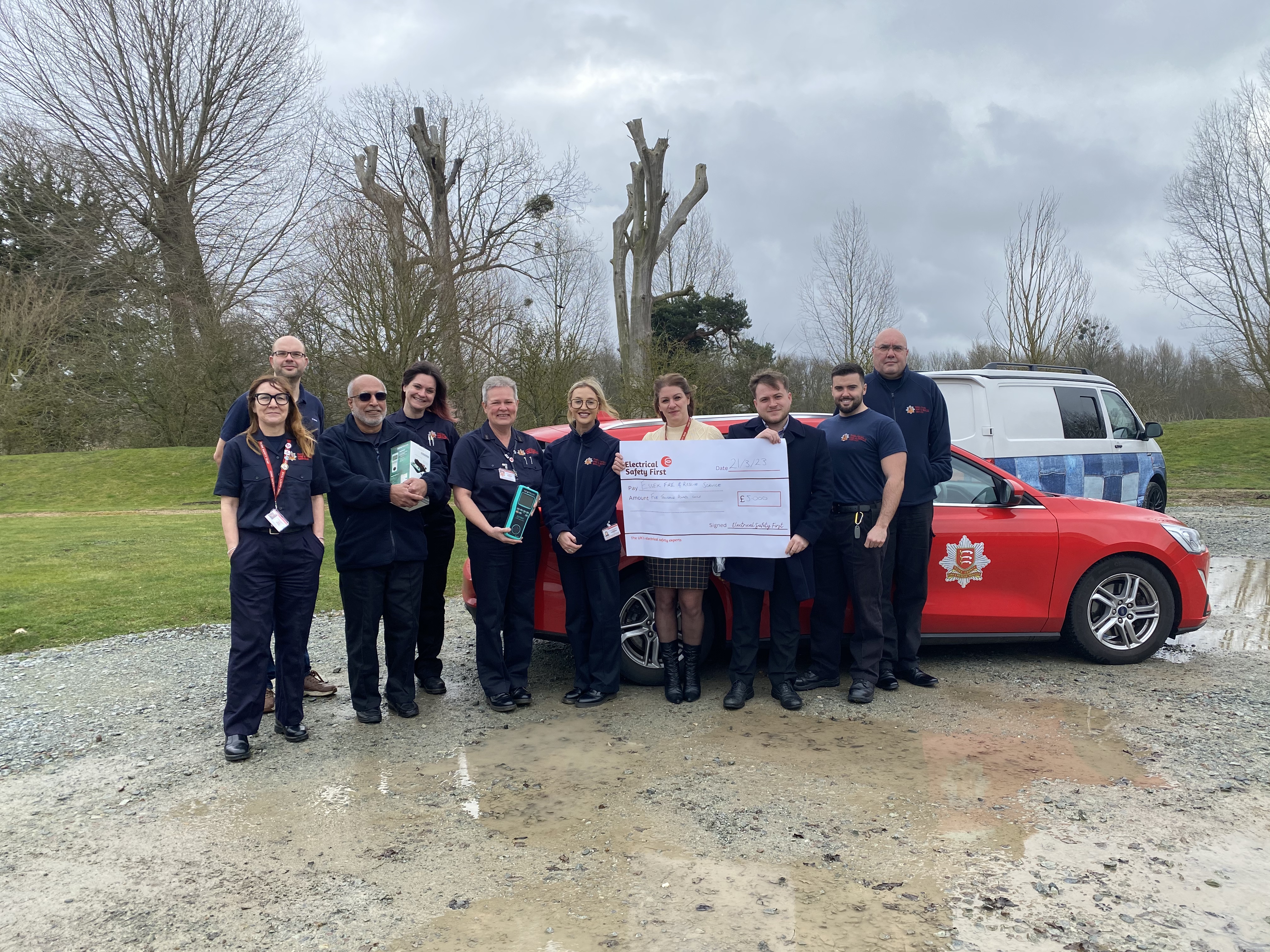 Members of the prevention team standing in front of a red car and holding a giant cheque