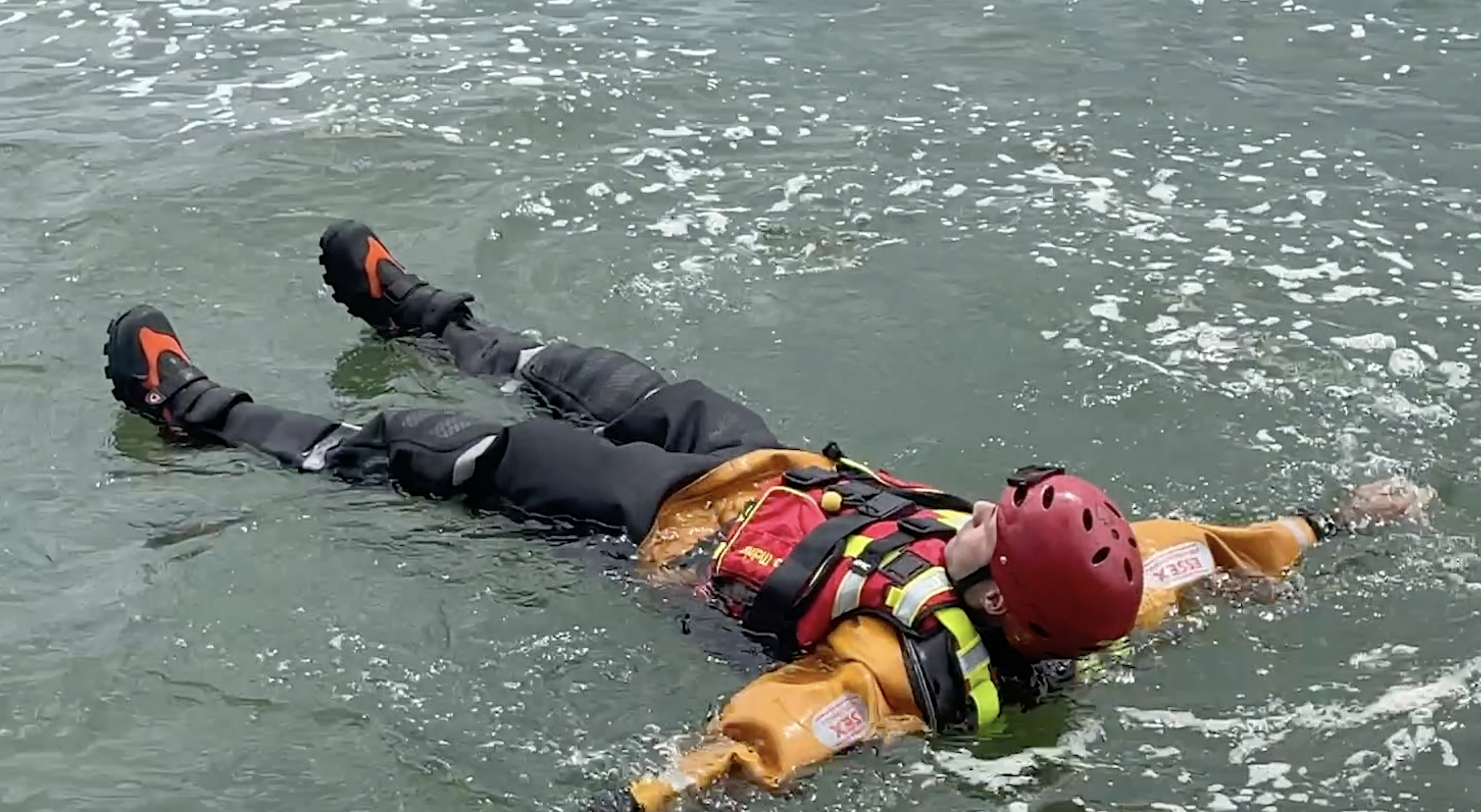 A firefighter floating on his back with his arms and legs stretched out in water to demonstrate how to float to live