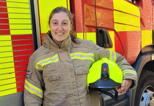 Firefighter Jennifer Adelle standing in front of a fire engine with her helmet