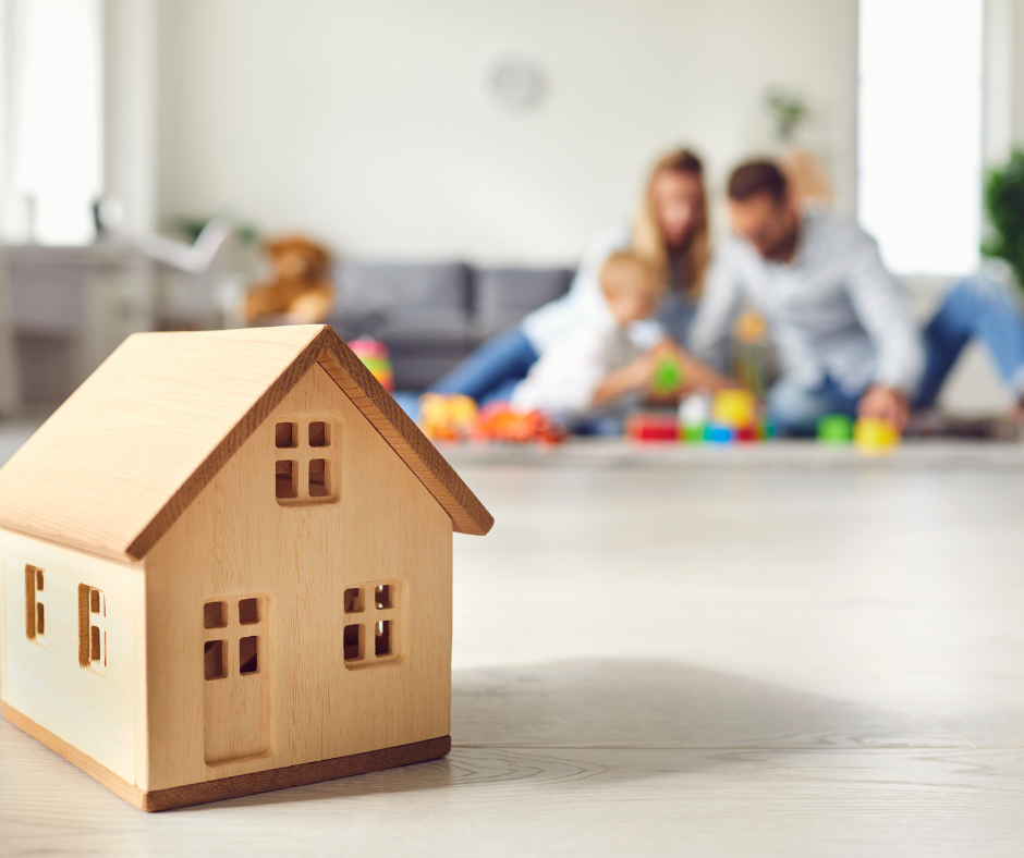 little toy wooden house in foreground and family in background