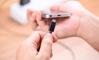 A hand holding a phone and the other hand placing a charger into the charging port