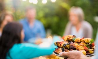 Plate of barbecued skewers being offered to group of friends in the distance