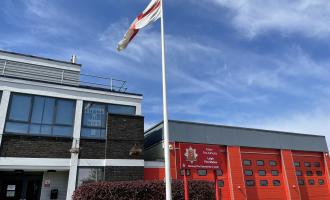 Fire Station building with three red shutter doors and a flag pole outside.