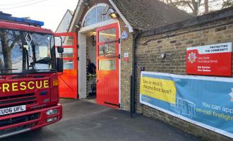 Small brick fire station building with one red shutter door. Fire Engine parked outside the front of building.