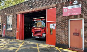 Small brick fire station building with one red shutter door. Fire engine visible inside.