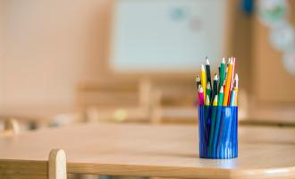 Blue pot filled with colouring pencils, set on wooden school desk