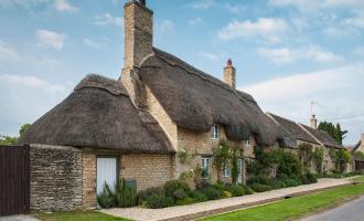 Thatched house with thatched garage. A grass verge separates the property from the road.