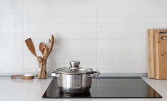 Stainless steel pan on induction hob. Wooden utensils and chopping board in the background