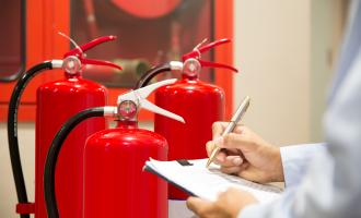 Three red fire extinguishers behind close up of man's arms holding a pen and a clipboard.