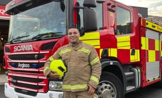 Dominic Daniel, on-call firefighter, stands in front of a fire engine.