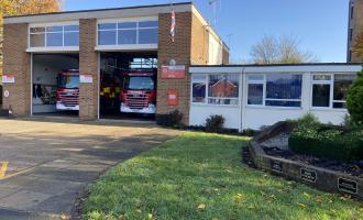 Brick fire station building with two bay doors and grass at the front