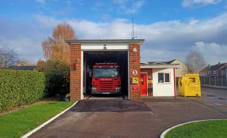 Small fire station building with one fire engine sitting inside a red bay door