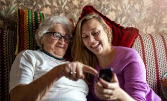 Young lady smiles at phone together with older lady