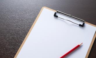 Clipboard on dark wooden table with red crayon laid on top