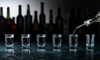 Bottle of spirit being poured into six shot glasses on bar