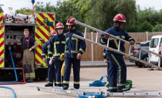 Four Fire Break participants, all boys in their teens, move a ladder across a forecourt at a fire station