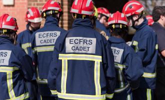 A group of teenage fire cadets pictured from behind, wearing navy PPE and red helmets