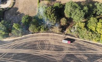 An aerial view of a burned field with a fire engine parked up.