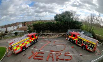Two fire engines parked with '75 years' written using fire hoses. 