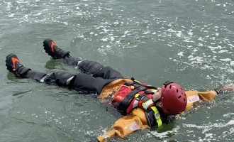 A firefighter floating on his back with his arms and legs stretched out in water to demonstrate how to float to live