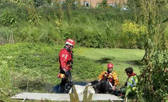A hose stuck in water in a field. Three people surround it, attempting a rescue,