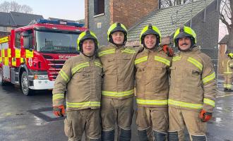 Four firefighters standing in the drill yard and smiling at the camera