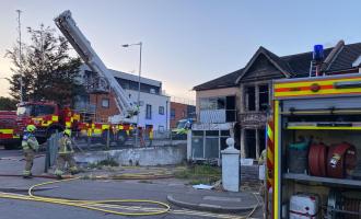 Two fire engines and firefighters next to a building affected by fire