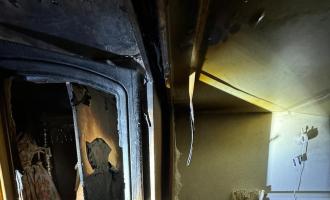 The inside of a fire damaged cupboard in a caravan with a cot next to it