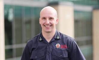 Chief Fire Officer Rick Hylton wearing a blue ECFRS shirt and standing in front of Fire HQ smiling at the camera
