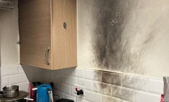 A kitchen with a scorched wall behind the cooker