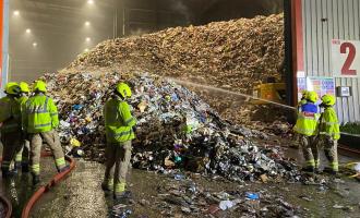 Two firefighters spraying water on a pile of rubbish in a warehouse, a more firefighter look on