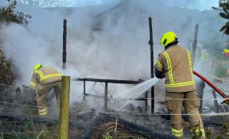 A firefighter spraying water on the charred remains of a stable